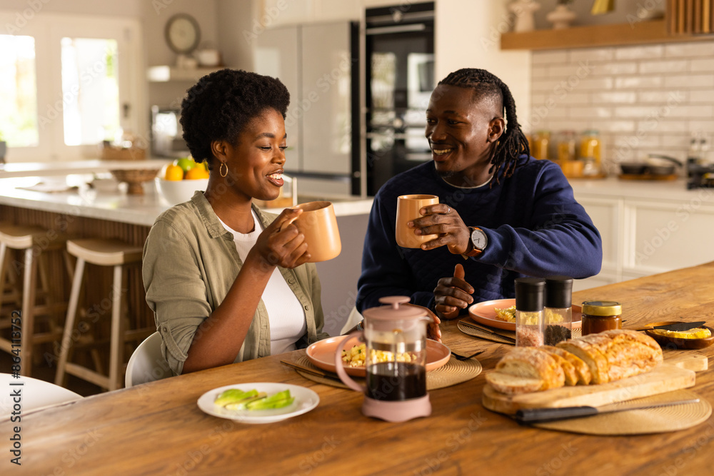 At home, Couple enjoying breakfast together, smiling and holding coffee mugs in kitchen At home, Couple enjoying breakfast together, smiling and holding coffee mugs in kitchen