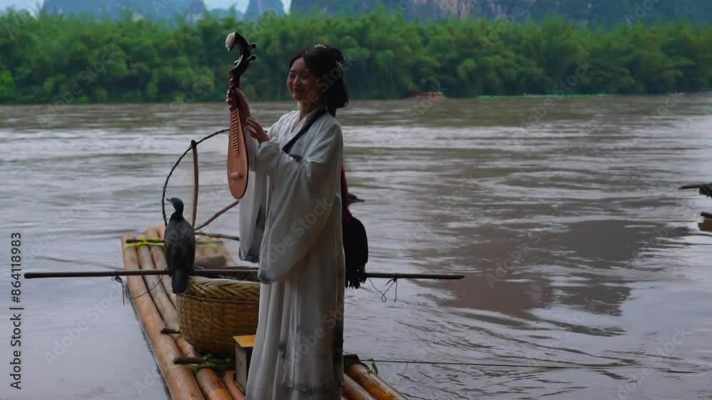 Playful Hanfu Asian girl poses with pipa on bamboo raft with Cormorant bird on wicker basket. Xingping, China Playful Hanfu Asian girl poses with pipa on bamboo raft with Cormorant bird on wicker basket. Xingping, China