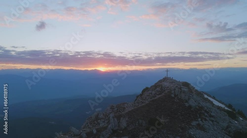 Drone shot of a man running on a mountain ridge at sunset. Sun setting and summit cross in the background. photo