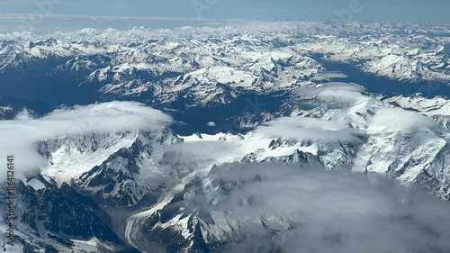 POV of The Alps Range, shot from an airplane cockpit while flying at 8000m high northbound. Daylight, with a few low clouds hiding the snowed peaks. 4K 60FPS. photo