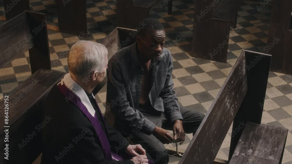 High angle view of African American man sitting in church, holding rosaries and having talk with senior Caucasian priest listening to him attentively High angle view of African American man sitting in church, holding rosaries and having talk with senior Caucasian priest listening to him attentively