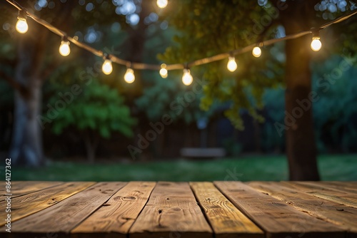 Empty Wood table top with decorative outdoor string lights hanging on trees in the garden at sunset time, blue, rad, green, yellow..