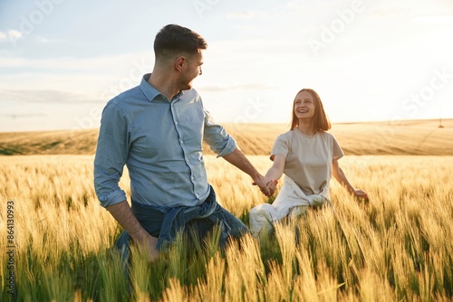 Leading the way, holding hands. Lovely beautiful couple are together on the agricultural field