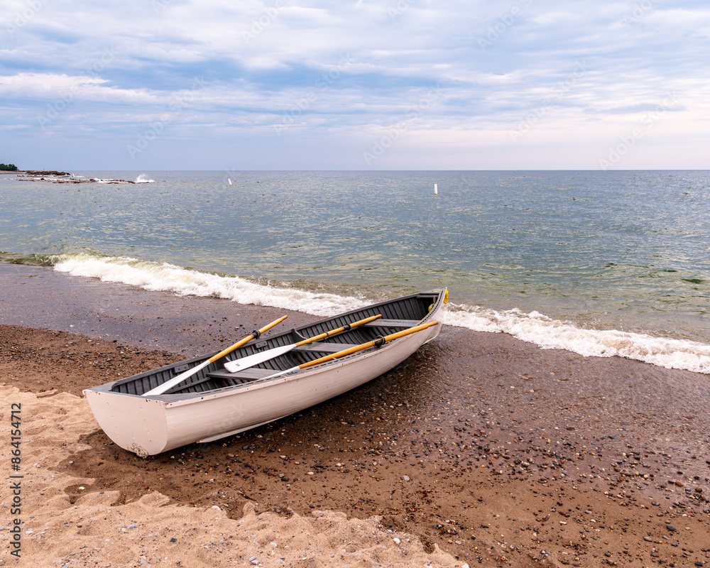 row boats at the waters edge on public beach with waves breaking on the sand green trees white clouds in a blue sky room for text shot on toronto's kew beach.