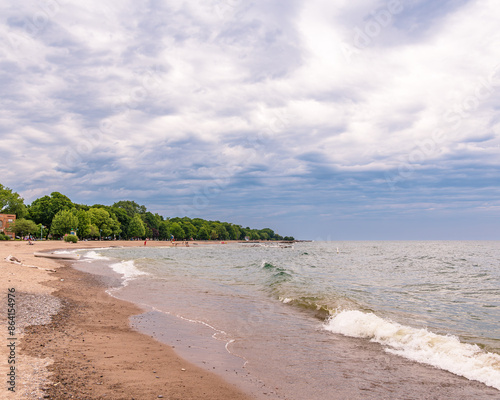Photography public beach with waves breaking on the sand green trees white clouds in a blue sky room for text shot on toronto's kew beach