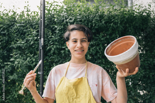 Happy and proud teenage girl showing the clay pot she is painting photo