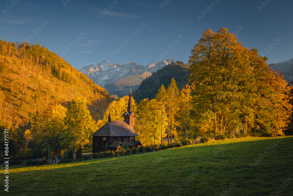 Autumn view of the Tatras in Slovakia: golden, red, and orange leaves on trees surround majestic mountains with snow-capped peaks. Clear, blue sky contrasts with the warm colors of the forest. Autumn view of the Tatras in Slovakia: golden, red, and orange leaves on trees surround majestic mountains with snow-capped peaks. Clear, blue sky contrasts with the warm colors of the forest.