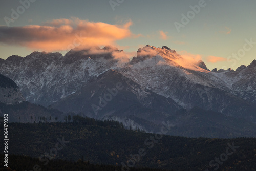 A beautiful autumn landscape of the Tatra Mountains seen from Polish Podhale during the golden hour. The sky is painted in warm hues, with the mountains bathed in golden light. © PawelUchorczak