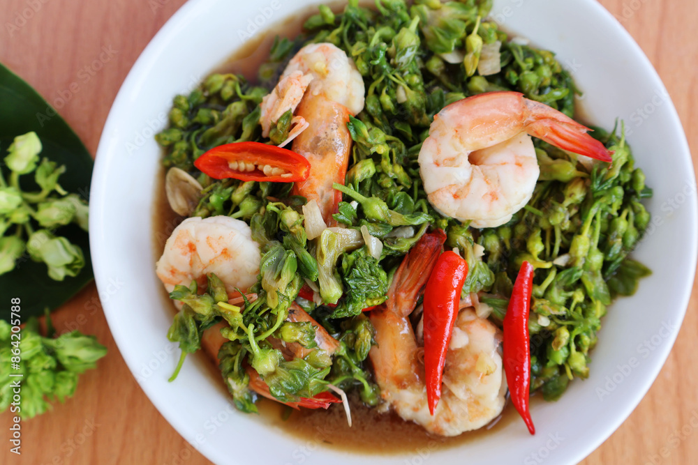 Stir-fry shrimp with green Telosma cordata flowers. Place sliced red chilies on top. In a white porcelain dish, placed on the table.
Stir-fry shrimp with green Telosma cordata flowers. Place sliced red chilies on top. In a white porcelain dish, placed on the table.