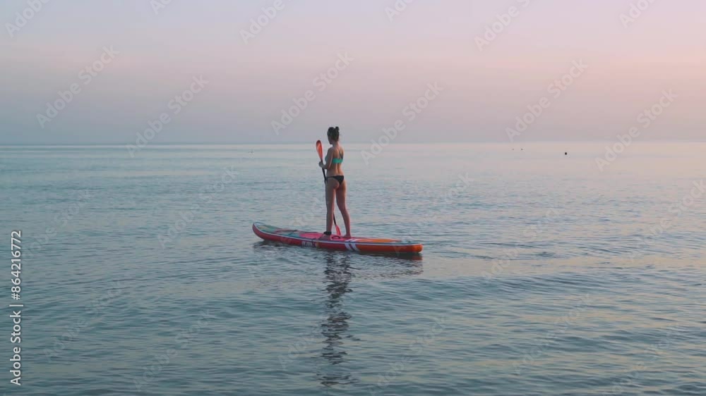 Vacation Woman in the Ocean Rowing an Oar While Standing on a SUP Board at Colored Sunset Slow Motion. Woman Swimming on SUP Board with Paddle in the Sea, Relax, Activity, SUP Boarding, Travel.