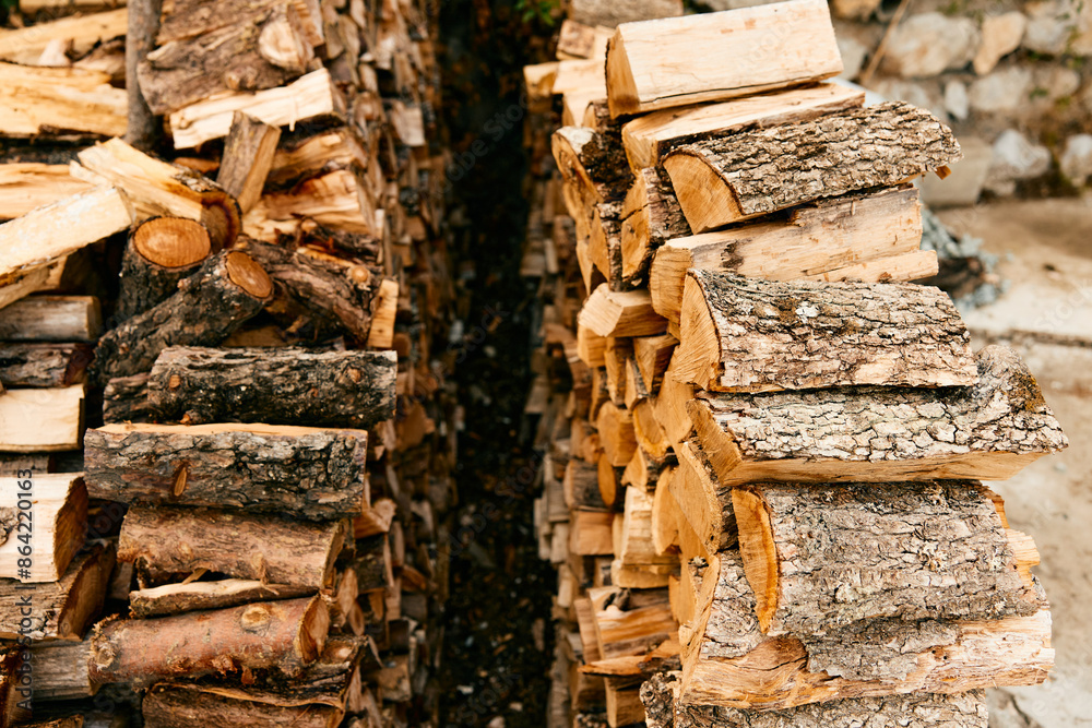 Rustic firewood stack against stone wall on a sunny day
