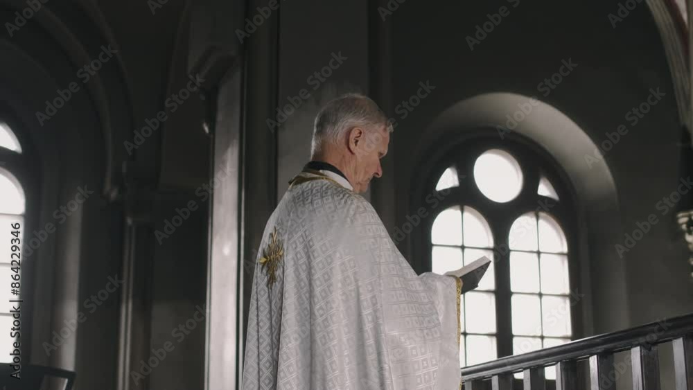 Arc shot of senior pastor in white robe reading Bible while standing on balcony in cathedral Arc shot of senior pastor in white robe reading Bible while standing on balcony in cathedral
