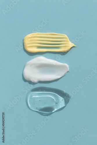 Smears of yellow, white cream and transparent gel or serum on a blue background. The texture of a cosmetic skin care product. Top view.