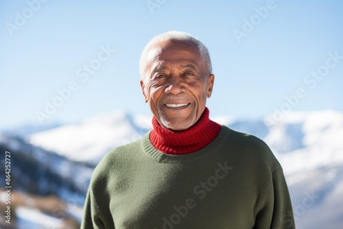 Portrait of a glad afro-american elderly man in his 90s wearing a classic turtleneck sweater in front of snowy mountain range © Markus Schröder