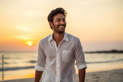 Portrait of a cheerful indian man in his 20s wearing a simple cotton shirt on beautiful beach sunset