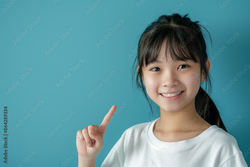 Playful Asian Girl Pointing with Cute Smile on Soft Blue Background for Clever Humor Concept Playful Asian Girl Pointing with Cute Smile on Soft Blue Background for Clever Humor Concept