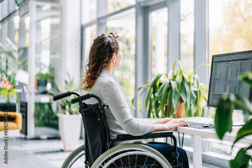 Side view of a young woman in a wheelchair using a computer in an office Concept of inclusion, diversity, accessibility and independence of people with reduced mobility. photo