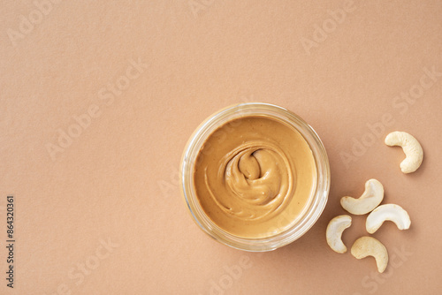 Nutritious cashew butter in glass jar and heap of nuts on table top view.