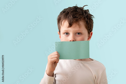 Young boy holding green card over mouth in studio