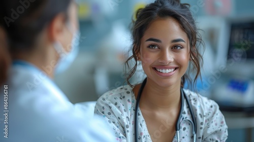 A young woman with a stethoscope, dressed in a hospital gown, sits and smiles at a doctor in her hospital room, indicating a positive medical consultation. photo