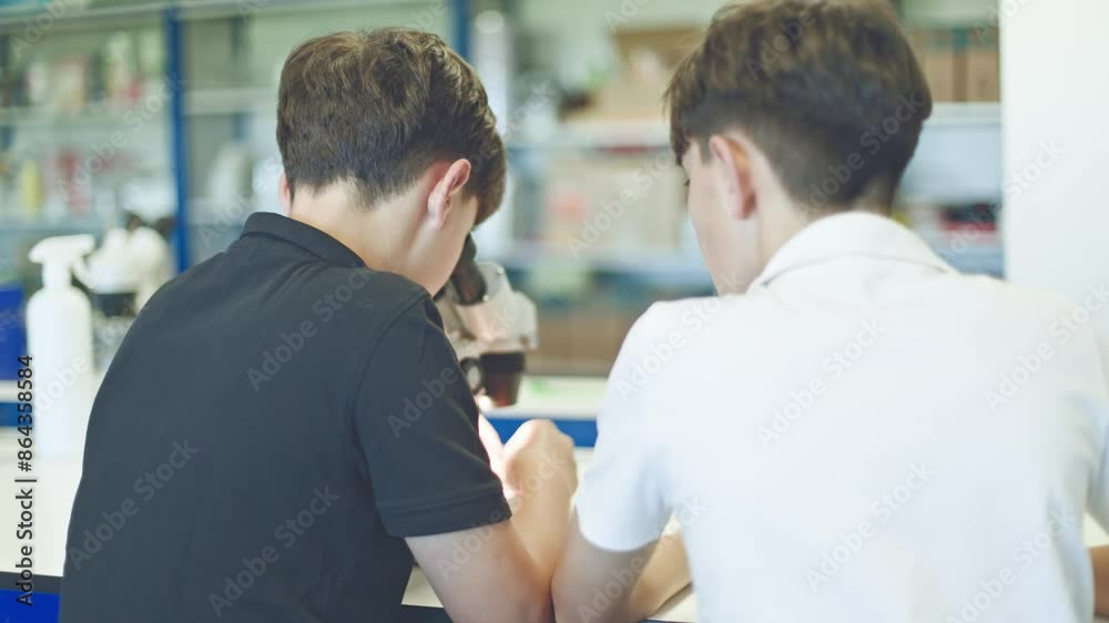 Two boys working together with a microscope in a science lab. Two boys working together with a microscope in a science lab.