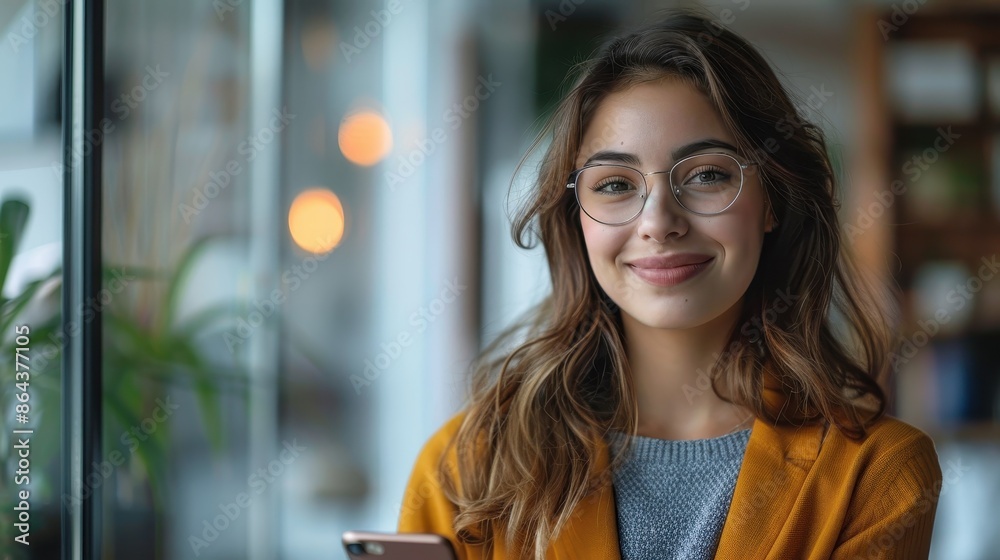 A smiling woman with glasses stands near a window, wearing a mustard-colored blazer, representing confidence and a cheerful demeanor in a bright office setting. A smiling woman with glasses stands near a window, wearing a mustard-colored blazer, representing confidence and a cheerful demeanor in a bright office setting.