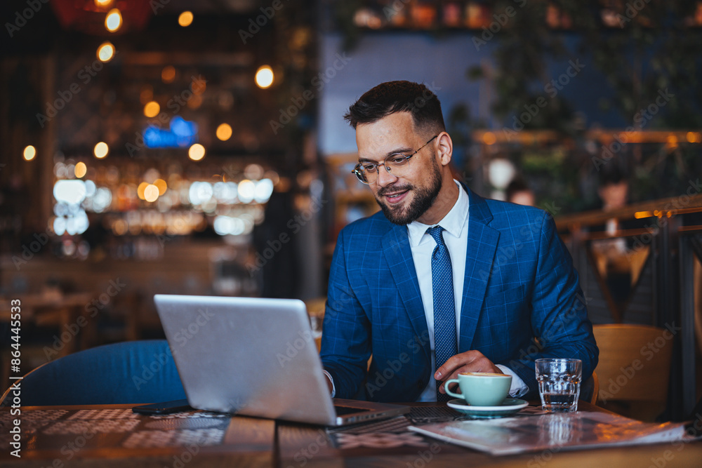 A cheerful man in a smart blue suit browses his laptop at a rustic coffee shop, a cup of coffee and glass of water by his side. A cheerful man in a smart blue suit browses his laptop at a rustic coffee shop, a cup of coffee and glass of water by his side.