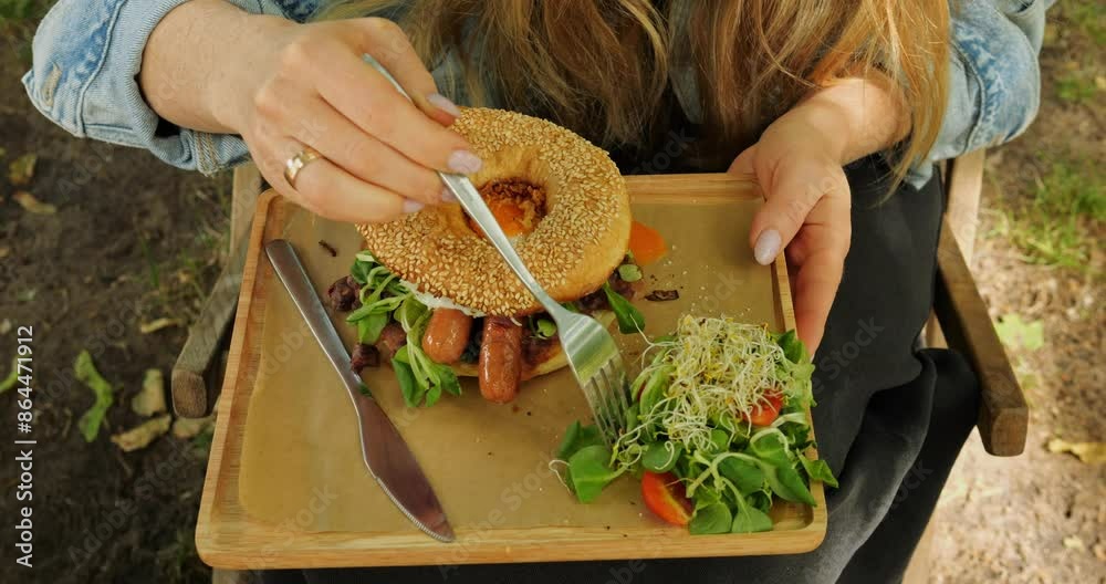 Burger served with green garnish on wooden board closeup. Nutritionally conscious woman has cheat meal on day off in public garden