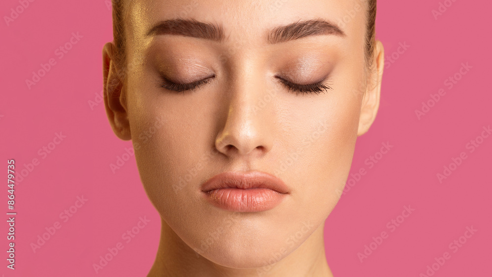 This is a close-up photo of a woman face with her eyes closed. The photo is taken against a pink background, and the focus is on the woman eyes, nose, and mouth. This is a close-up photo of a woman face with her eyes closed. The photo is taken against a pink background, and the focus is on the woman eyes, nose, and mouth.