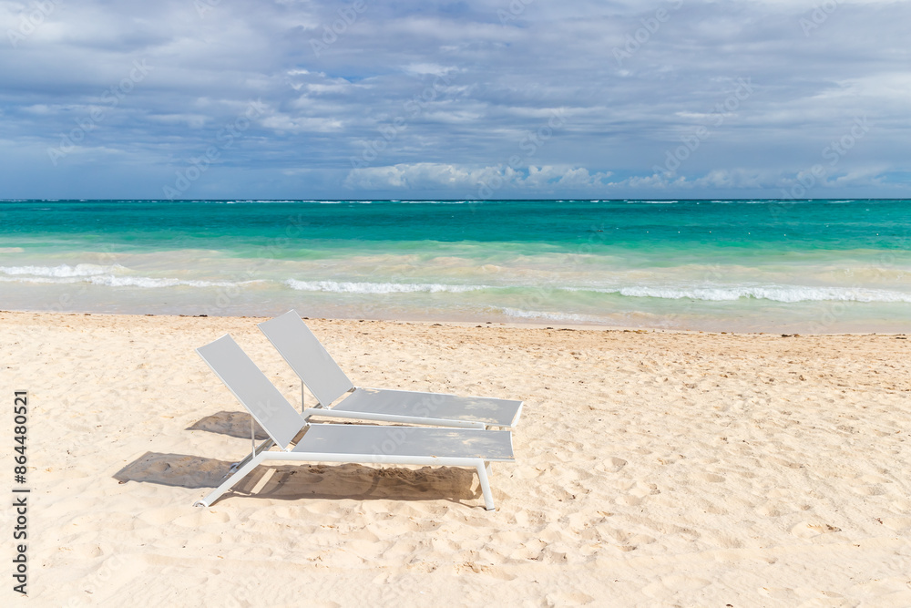 Two vacant sun loungers are on the beach on a sunny day Two vacant sun loungers are on the beach on a sunny day