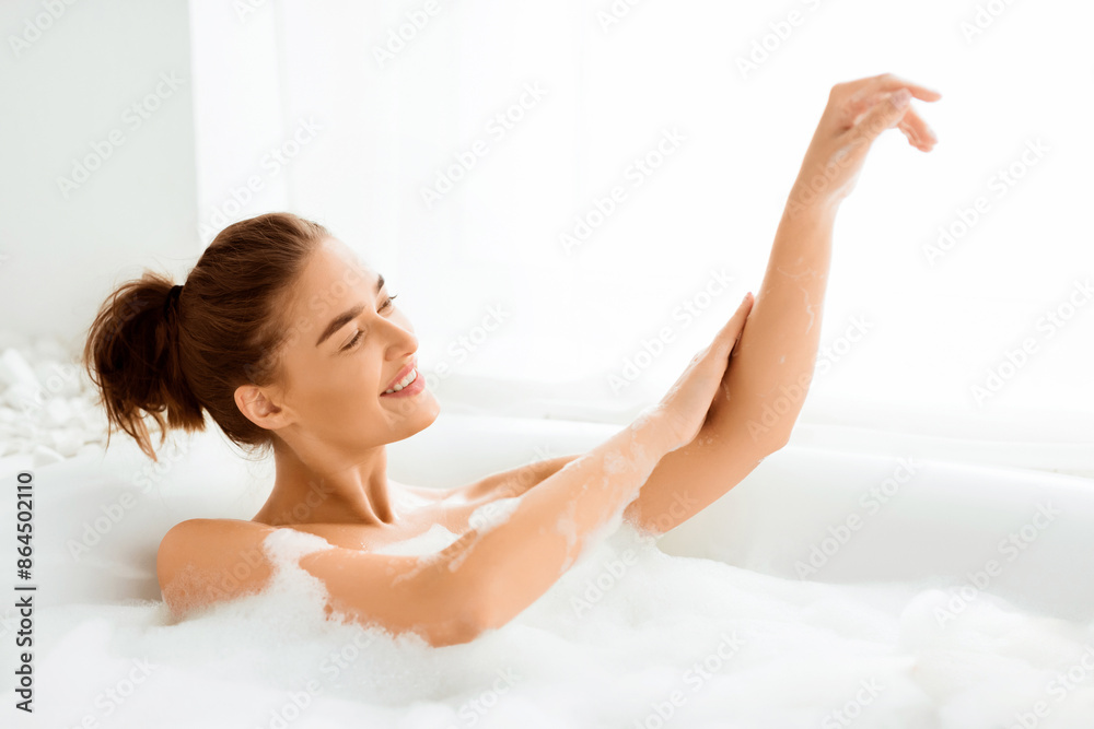 Beautiful woman enjoying pleasant bath with foam, applying cream on hands Beautiful woman enjoying pleasant bath with foam, applying cream on hands