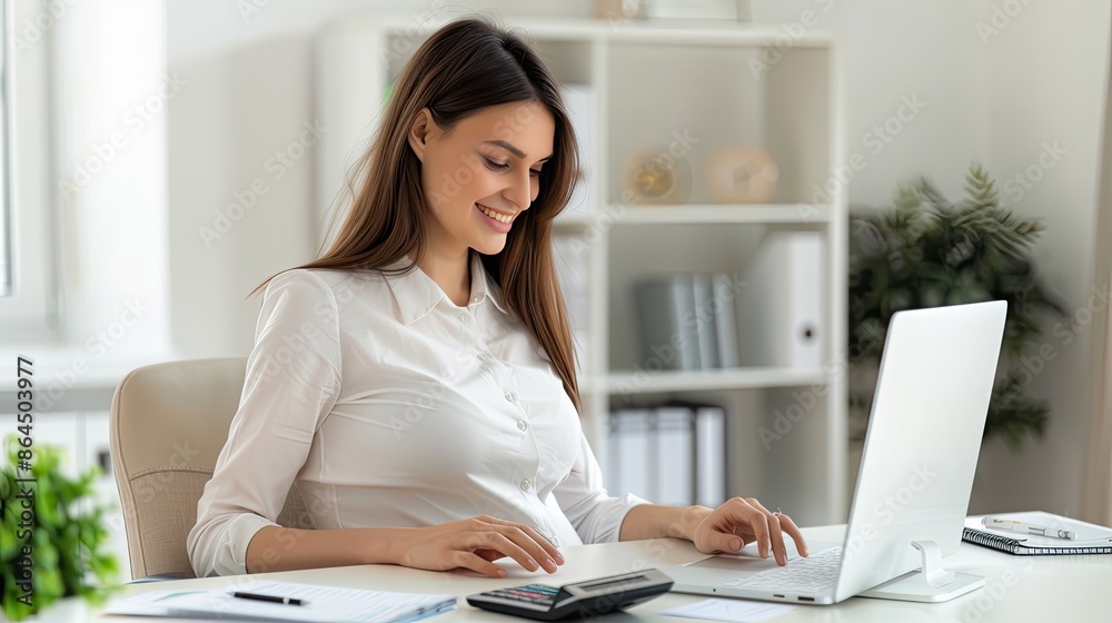 A young businesswoman sits at her desk, smiling while working on her laptop in a modern office setting A young businesswoman sits at her desk, smiling while working on her laptop in a modern office setting