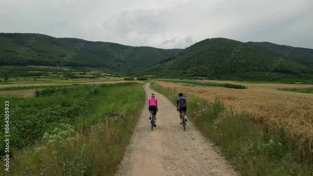 Gravel cycling in field. Woman a man cyclists are riding gravel bikes on country road through farm field. Gravel cycling in field. Woman a man cyclists are riding gravel bikes on country road through farm field.