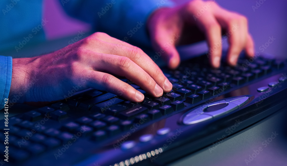 A close up image of a persons hands typing on a black computer keyboard. The keyboard has a built-in mouse pad. The image is lit by purple and blue light, giving it a futuristic or techy feel. A close up image of a persons hands typing on a black computer keyboard. The keyboard has a built-in mouse pad. The image is lit by purple and blue light, giving it a futuristic or techy feel.