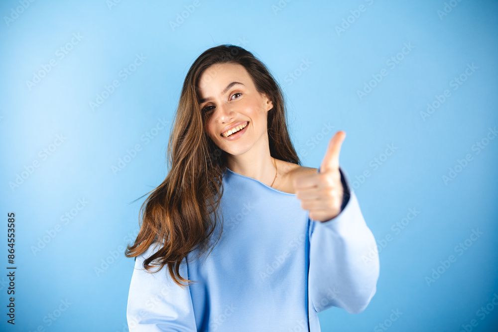 Optimistic brunette hair woman makes thumbs up gives approval shows excellent gesture says nice job gives positive feedback shares good opinion, wow, wear blue top isolated over blue background. Optimistic brunette hair woman makes thumbs up gives approval shows excellent gesture says nice job gives positive feedback shares good opinion, wow, wear blue top isolated over blue background.