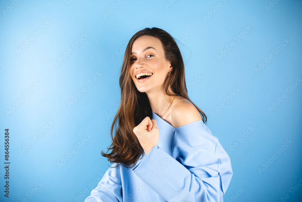 Photo of pretty brunette woman wear blue pullover champion winking eye raising fist well done job standing side isolated blue color background. Girl show win wow gesture. Photo of pretty brunette woman wear blue pullover champion winking eye raising fist well done job standing side isolated blue color background. Girl show win wow gesture.