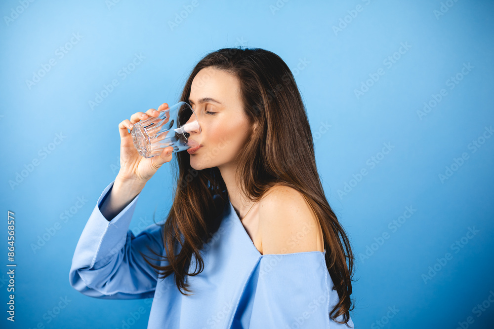 Young woman wear blue pullover hold transparent glass drink clear fresh pure still water close eyes isolated on blue background. Proper nutrition healthy fast food choice concept. Young woman wear blue pullover hold transparent glass drink clear fresh pure still water close eyes isolated on blue background. Proper nutrition healthy fast food choice concept.