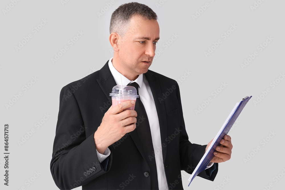 Mature businessman with glass of fruit smoothie and clipboard on light background Mature businessman with glass of fruit smoothie and clipboard on light background