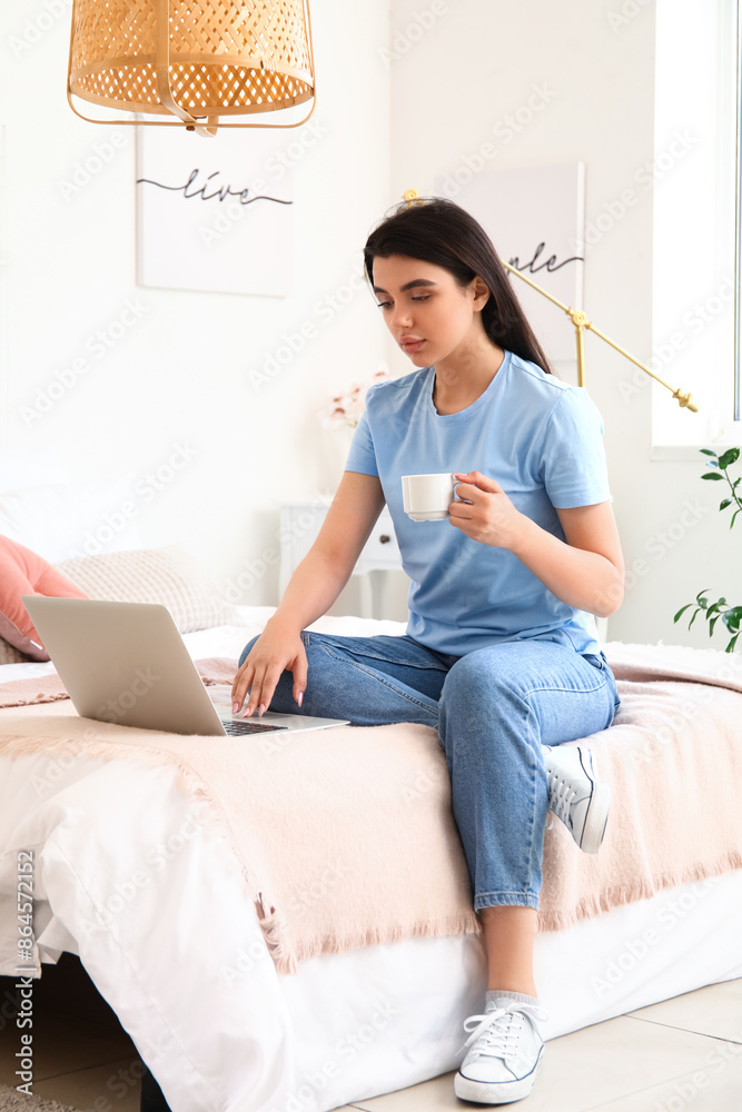 Female freelancer with cup of coffee working online in bedroom Female freelancer with cup of coffee working online in bedroom