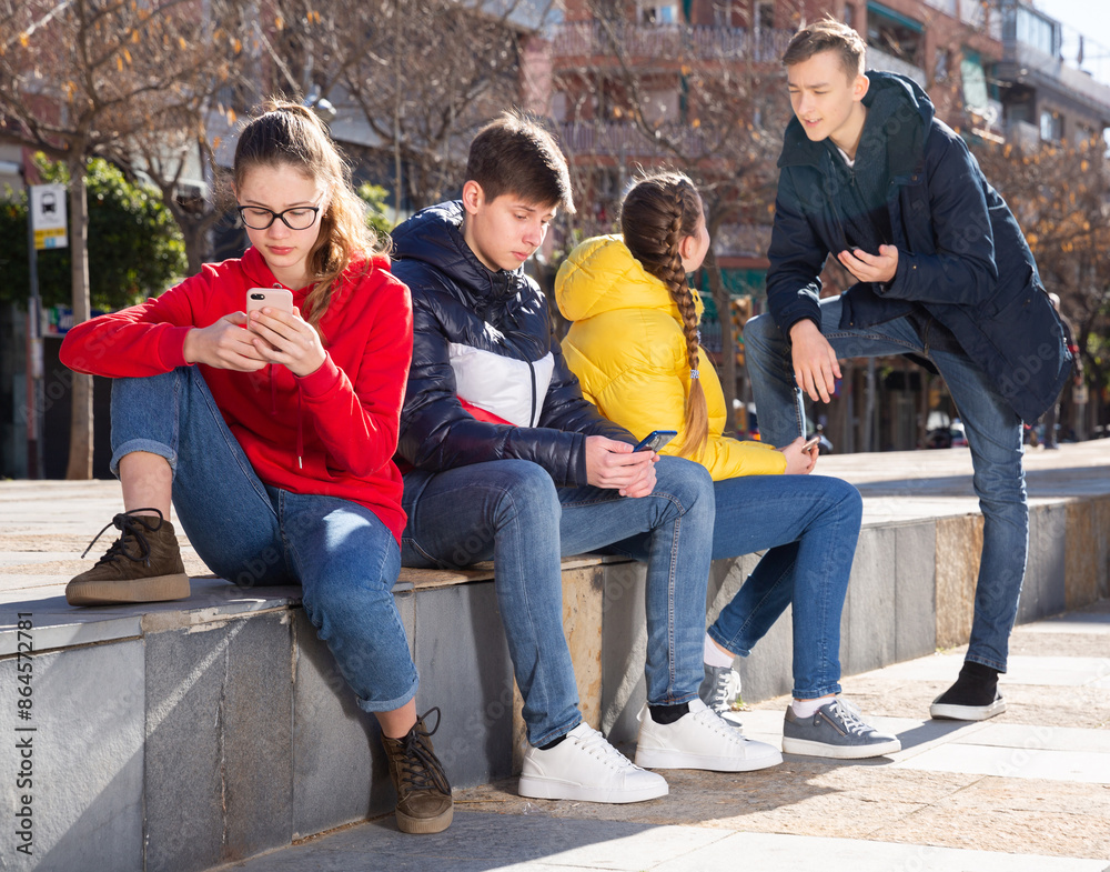 Fototapeta premium Teenage friends spending time together in city streets in spring, discussing interesting topics and browsing on phones