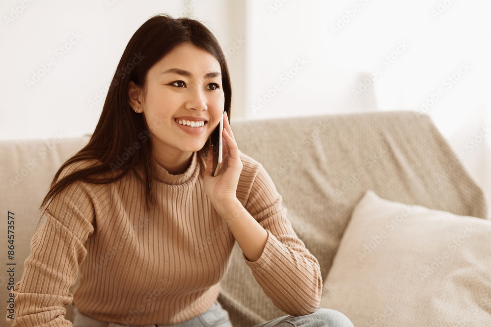 Asian Girl Talking on Mobile Phone and Smiling, Sitting on Couch at Home, Free space Asian Girl Talking on Mobile Phone and Smiling, Sitting on Couch at Home, Free space