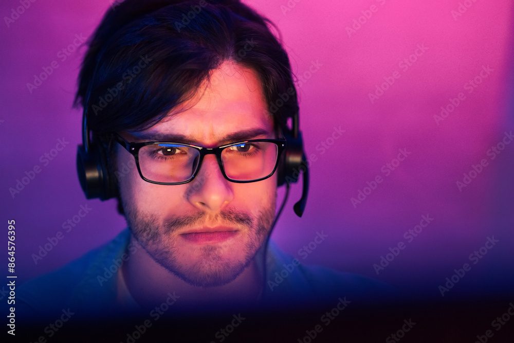 This image shows a young man with dark hair wearing glasses and headphones while looking at a computer screen. He has a serious expression on his face, suggesting he is focused on his task. This image shows a young man with dark hair wearing glasses and headphones while looking at a computer screen. He has a serious expression on his face, suggesting he is focused on his task.