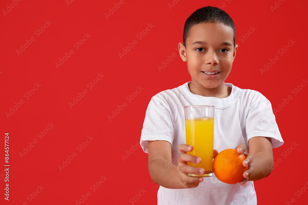 Little African-American boy with glass of juice and orange on red background Little African-American boy with glass of juice and orange on red background