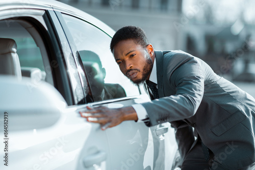 Fotografie African American man in a suit is inspecting a white car during the day