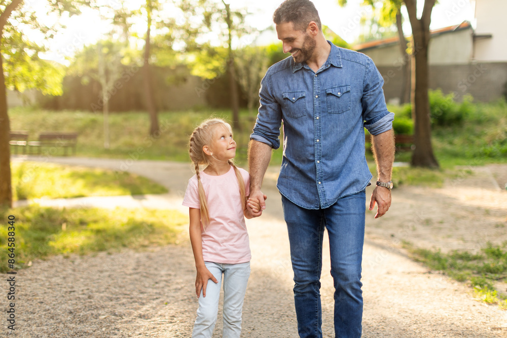 A father and his young daughter walk hand-in-hand on a gravel path through a park. The sun shines brightly, casting long shadows on the ground. They are both smiling, enjoying the beautiful day A father and his young daughter walk hand-in-hand on a gravel path through a park. The sun shines brightly, casting long shadows on the ground. They are both smiling, enjoying the beautiful day
