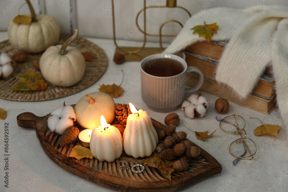 Composition with burning candles, cup of tea and autumn decor on light table Composition with burning candles, cup of tea and autumn decor on light table