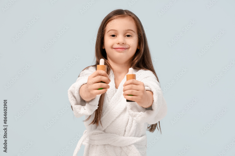 Cute little happy girl in bathrobe with bottles of cosmetic oil on blue background Cute little happy girl in bathrobe with bottles of cosmetic oil on blue background