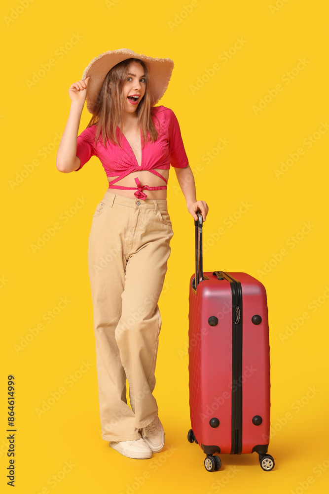Beautiful young woman with suitcase on yellow background