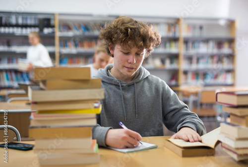 Portrait of teenager reading books and writing in notebooks in the library photo