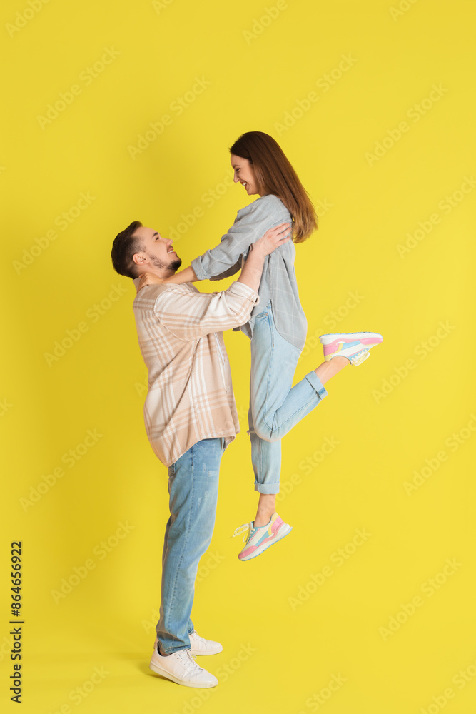 Happy man lifting his girlfriend on yellow background Happy man lifting his girlfriend on yellow background